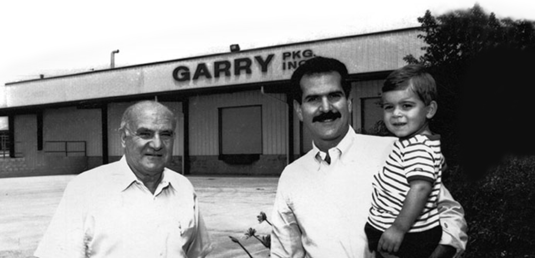 Black and white photo showing three generations of the Garry family in front of their building